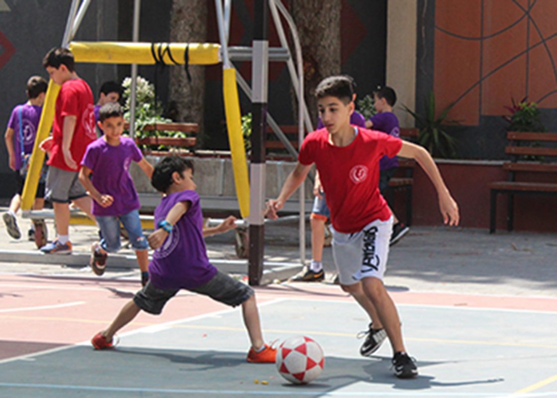 Children laughing and playing outdoor games at a summer camp in Gaza, with camp counselors looking on