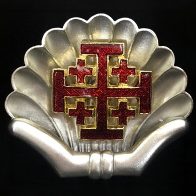 A Pilgrim Shell badge with the Jerusalem Cross at its center, displayed against a dark background